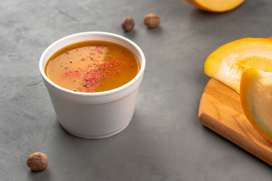 Pumpkin soup with seasonings in a disposable plate near the gray table