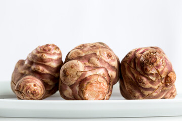 Three Jerusalem artichokes (Helianthus tuberosus), also known as sunroot, sunchoke, or earth apple, on a white plate, and against a white background. Horizontal front view.