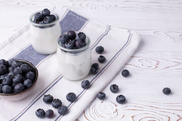 A healthy breakfast of Greek yogurt in glass jars and fresh blueberries at a rustic white table. Selective focus on glass jar in front with blurred background.