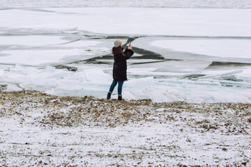 Cracked ice, lots of pieces of ice on the river. Girl is take the photo of landscape. 