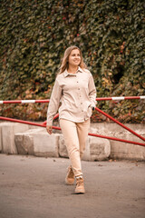 A pretty blonde young woman is walking down the street, she is wearing jeans and a beige shirt. Beautiful girl dressed in casual style with a smile on her face for a walk