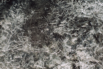 Close up of pattern cracks on the dark ice surface of the lake in winter