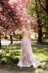woman's day. beautiful young woman in luxury long dress near blossoming of sakura. stylish girl near blossoming sakura flowers on background in the spring park. Harmony with nature concept © Andriy Medvediuk