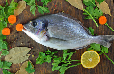 Fresh Dorado fish and spices bay leaf, parsley, pepper, carrots lie on a wooden table.