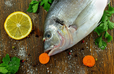 Fresh Dorado fish and spices bay leaf, parsley, pepper, carrots lie on a wooden table.