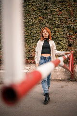 A pretty redhead young woman is walking down the street, she is dressed in jeans and a beige shirt. Beautiful girl dressed in casual style with a smile on her face