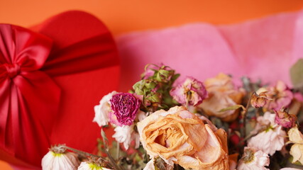 Close up of bouquet of wilted flowers with red gift box. Variety of withered flowers in wrapping paper with present in form of heart.