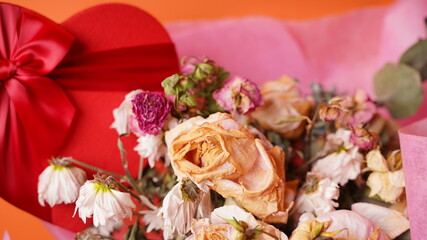 Close up of bouquet of wilted flowers with red gift box. Variety of withered flowers in wrapping paper with present in form of heart.
