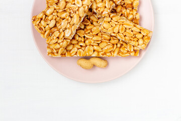 Peanut brittle candies in honey caramel on plate on white background