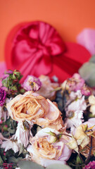 Close up of bouquet of wilted flowers with red gift box. Variety of withered flowers in wrapping paper with present in form of heart.