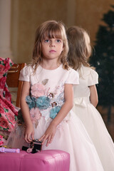 cute little blond baby girl with long hair choose dress for Christmas night full body photo