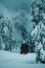 The famous Brocken train with steam in the winter mountain landscape with heavy fog and mystic vibes. Steam historic train, Brockenbahn, up the snow hill. Brocken, Harz National Park in Germany
