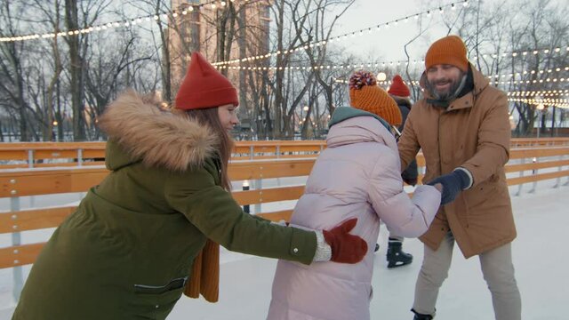 Handheld tracking slow-motion footage of young happy family of three ice-skating in train formation on winter evening at sunset