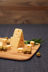 A piece of cheese with holes and olives on a wooden board. Maasdam cheese.