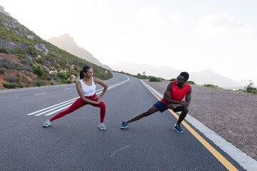 Fit african american couple in sportswear stretching on a coastal road