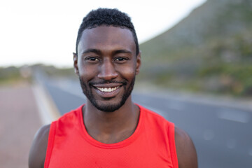 Portrait of fit african american man standing on a coastal road looking at camera smiling