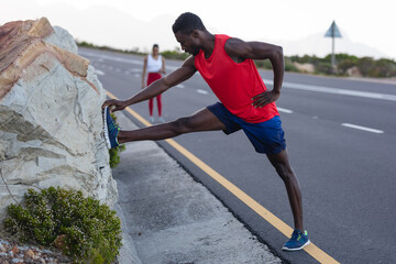 Fit african american man in sportswear stretching on a coastal road