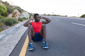 Fit african american man in sportswear doing crunches on a coastal road