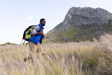 Fit afrcan american man wearing backpack hiking in mountain countryside