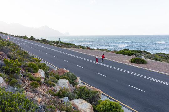 Fit african american couple in sportswear running on a coastal road - Powered by Adobe