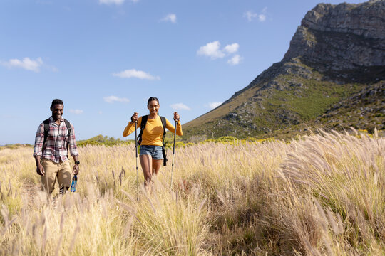 Fit afrcan american couple wearing backpacks nordic walking with poles in mountain countryside