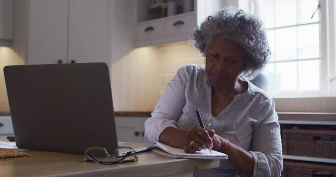 Senior african american woman using laptop and taking notes at home