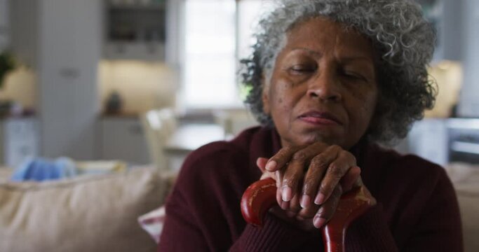 Thoughtful senior african american woman holding walking stick sitting on the couch at home
