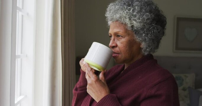 Senior african american woman drinking coffee and looking out of the window at home