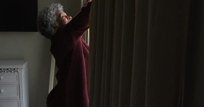 Senior african american woman opening curtains of the window at home