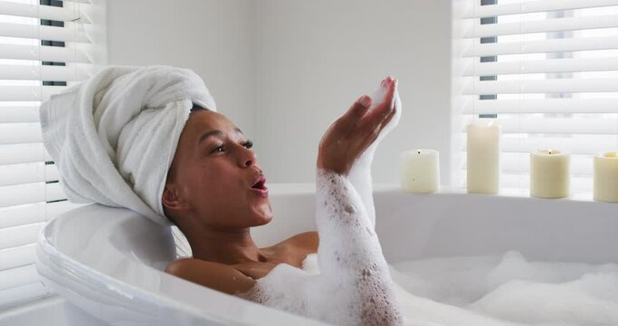 African american woman blowing soap bubbles in the bath tub in the bathroom at home