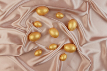 Golden decorative Easter eggs on a background of creamy shiny natural fabric. Soft texture concept. Champagne silk fabric.