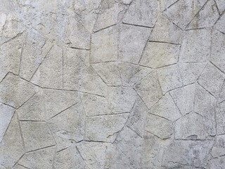 A gray concrete wall with peeling decorative rough plaster with a geometric pattern. Imitation of masonry. Texture not seamless