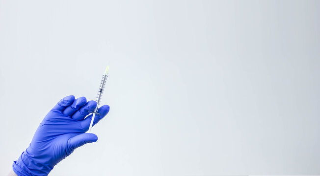 Hand in blue the glove holds a plastic syringe with liquid for injection. Vaccination concept. Healthcare, treatment concept.