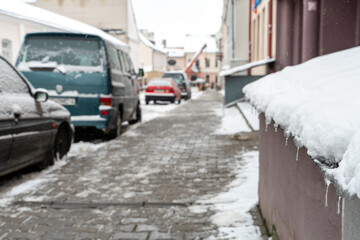 Fototapeta premium the facade of buildings after a snowfall is covered with snow and icicles. Parked cars are covered in snow and ice. Ice on roads and sidewalks. Danger of falling on slippery surfaces.