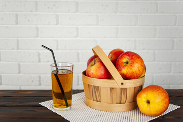beautiful apples in a wooden basket on a wooden surface and a glass of apple juice