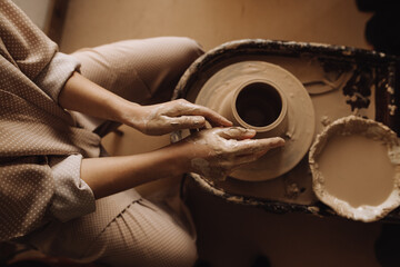 hands of a girl with clay next to a vase on a potter's wheel