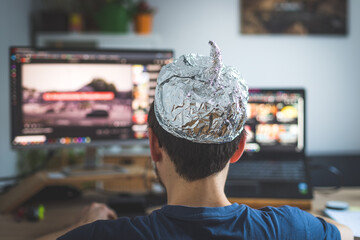 Conspiracy theory concept: young man is wearing aluminum head, sitting in front of the pc watching videos