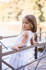 Portrait of a little girl outdoors in the summer by the lake. Little girl in summer dress by the river.