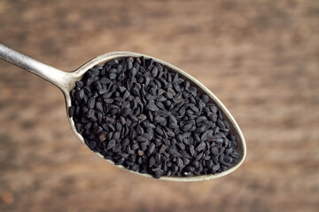 Black cumin seeds on a metal spoon, top view