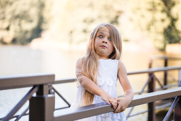 Portrait of a little girl outdoors in the summer by the lake. Little girl in summer dress by the river.