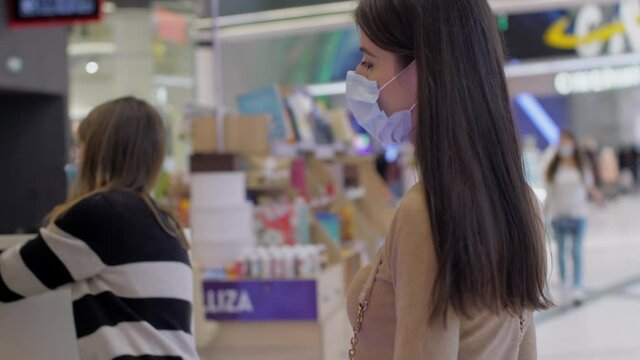 Long haired brunette in blue disposable face mask looks around walking along department store with bookshelves