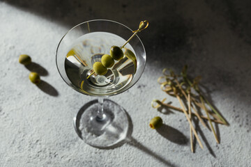 Glass of classic dry martini cocktail with olives on grey stone background.