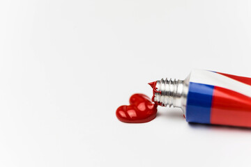 Small aluminum tube with red acrylic paint, heart shaped embossed paint on white sheet of paper, close-up view, love concept
