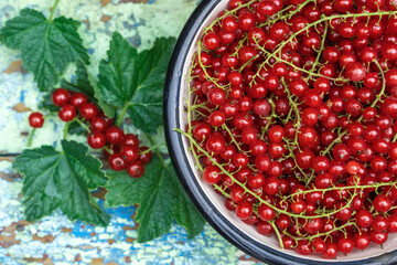 Berries of a red currant in a metal bowl on a old wooden background in a rustic style. Flat lay, top view, close-up.