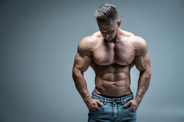 young handsome sportsman bodybuilder posing in jeans on grey background - obrazy, fototapety, plakaty