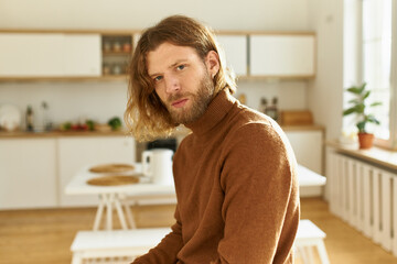 Home, interior, people and lifestyle concept. Handsome young man with beard and ginger hair...