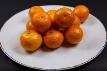 Large textured plate with tangerines, on a black background.