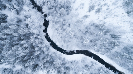 Aerial view of river thorugh snow covered forest in calm scene.  Drone view photo from the drone on a cloudy day. Aerial top view beautiful snowy landscape.
 - Powered by Adobe