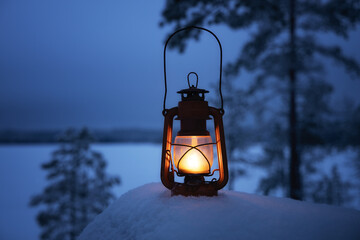 Glowing lantern in winter evening forest. Beautiful winter background. Snow covered lake and pine trees. Holiday concept. 
 - Powered by Adobe