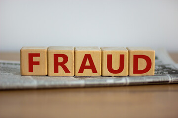Obraz premium Fraud symbol. Wooden cubes placed on a newspaper. The word 'fraud'. Beautiful wooden table. White background. Business and fraud concept. Copy space.